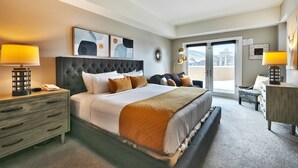 Quarto de hotel com uma cama grande, uma mesa de cabeceira, cômoda e vista para a cidade pela janela.