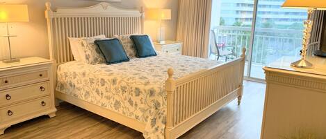 A bedroom with a large bed, two bedside tables, a nightstand, a dresser, a window with curtains, and a view of buildings.