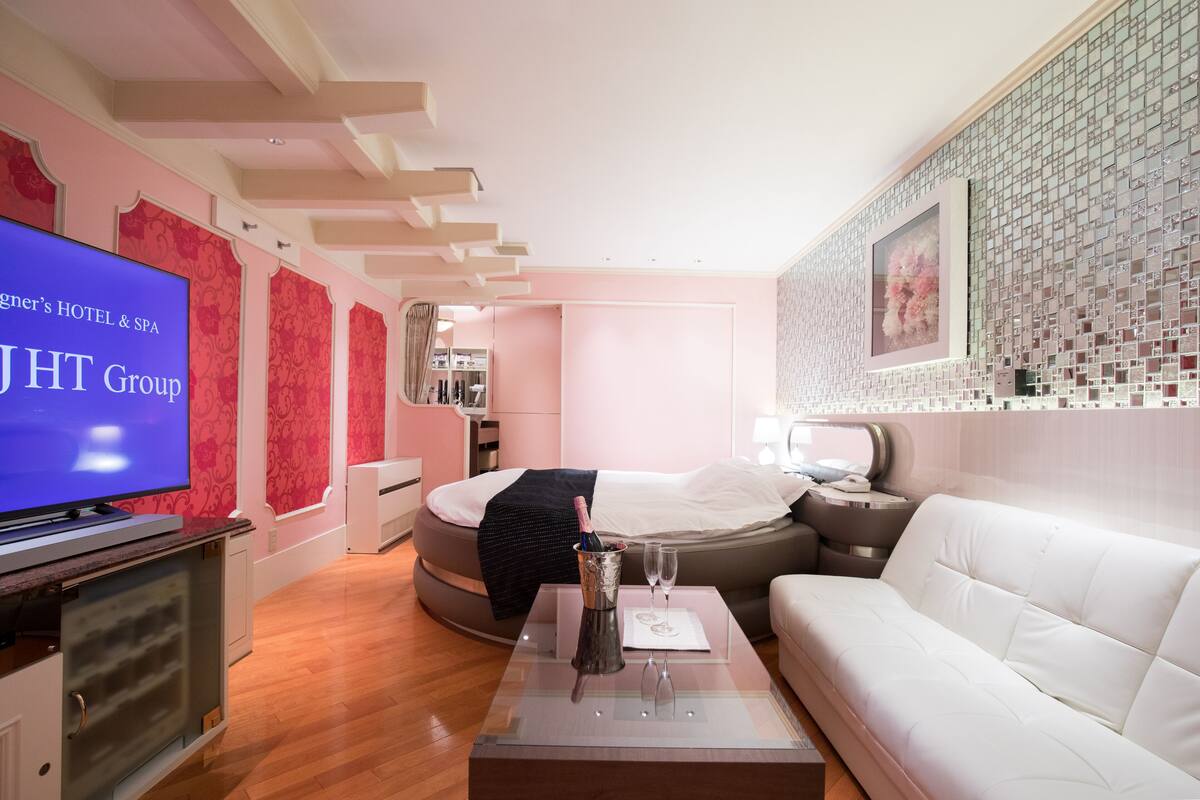 A modern hotel room with a bed, a white sofa, a TV, and a minibar.