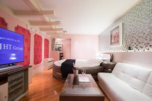 Una habitación de hotel moderna con una cama, un sofá blanco, un televisor y un minibar.