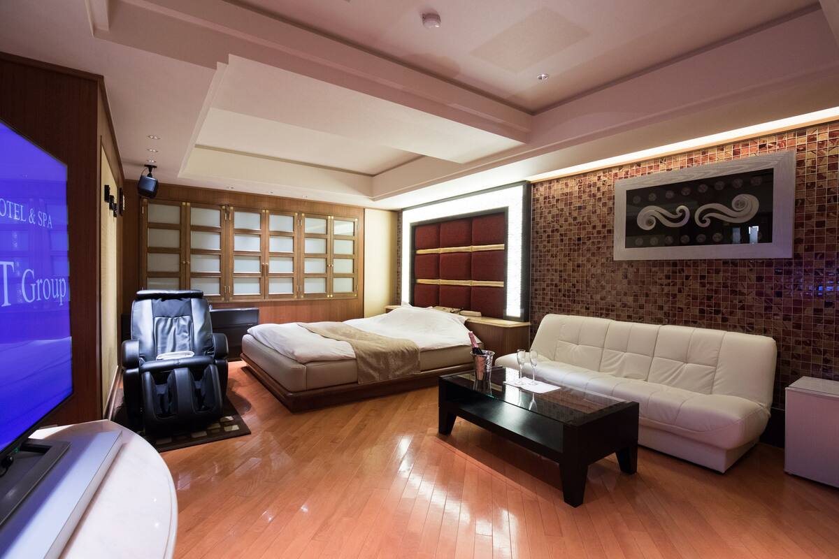 A modern hotel room with a massage chair, a sofa, a flat-screen TV, and a large window.