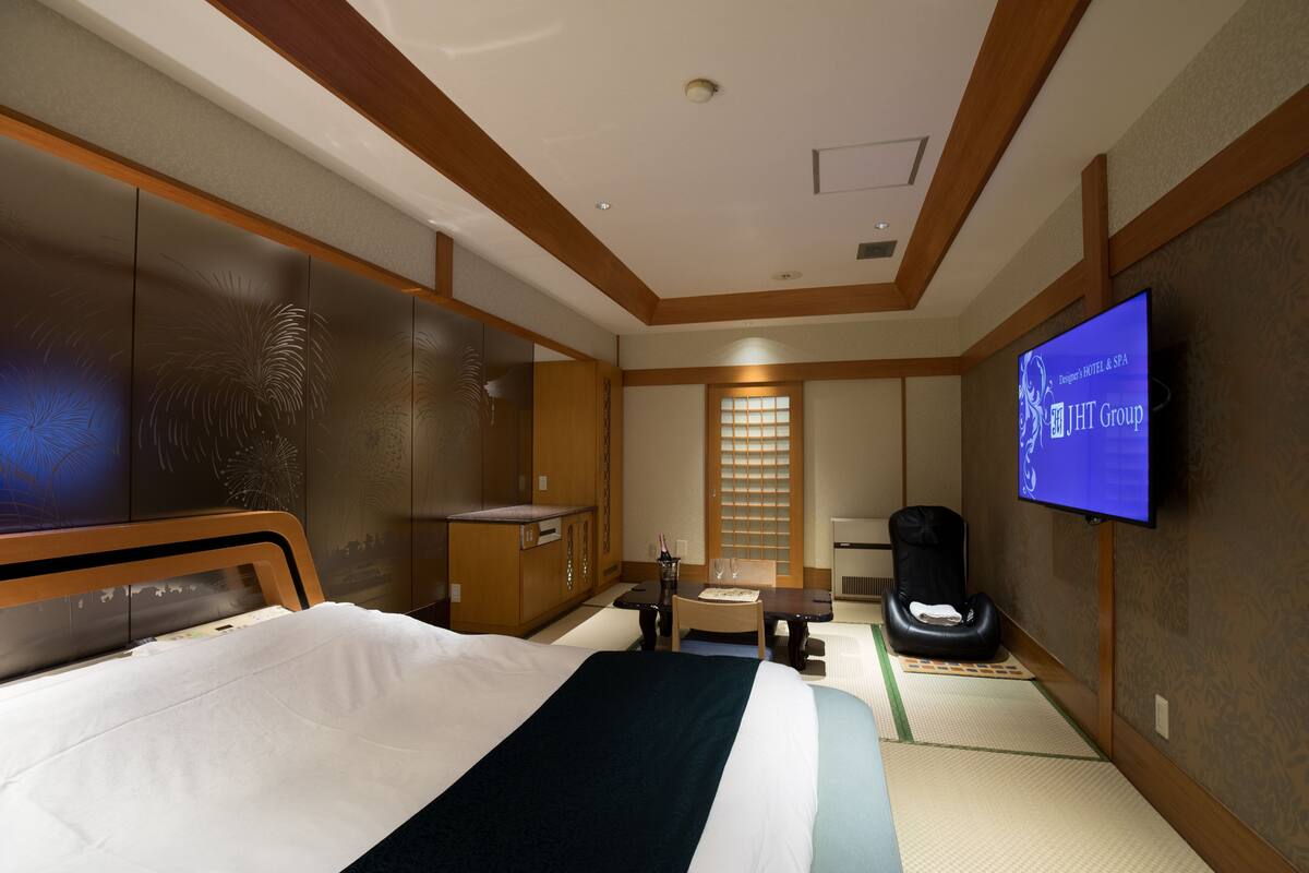 A hotel room with a bed, a desk, a chair, a television, and a massage chair.