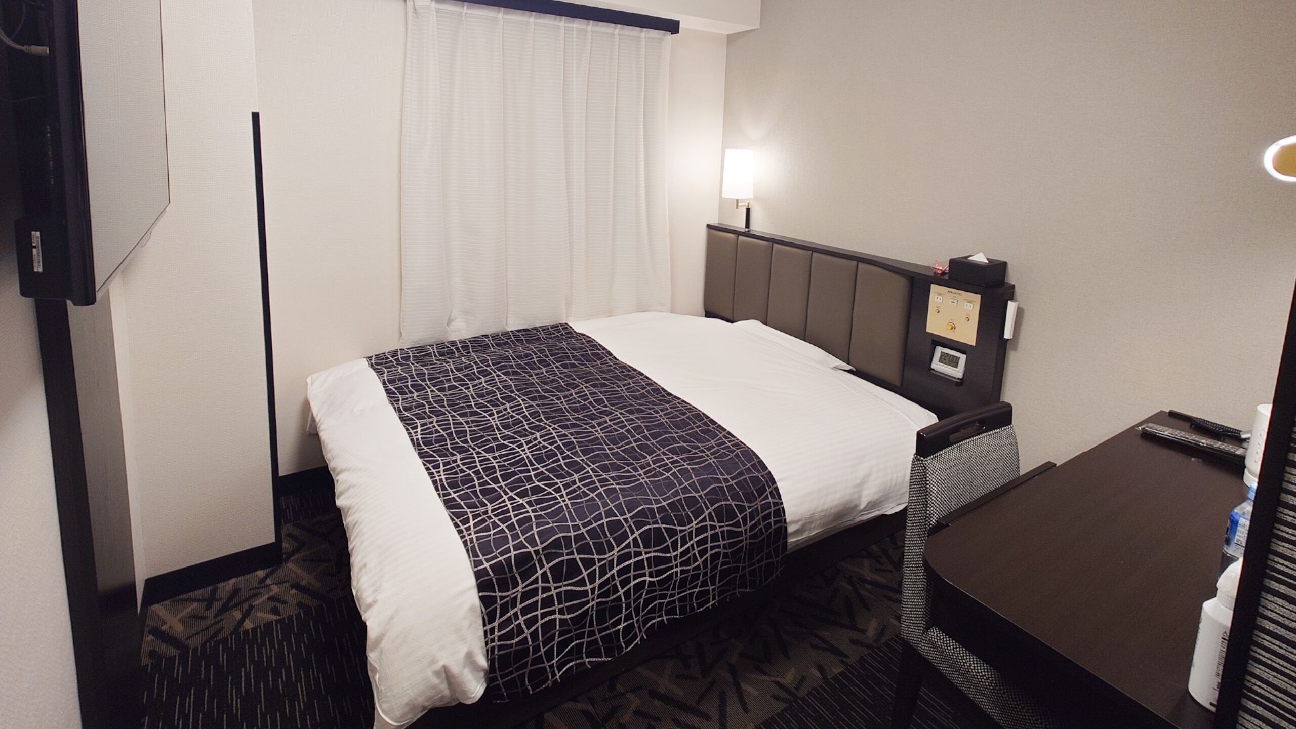 Ein Hotelzimmer mit Bett, Nachttisch, Lampe und Bedienfeld.