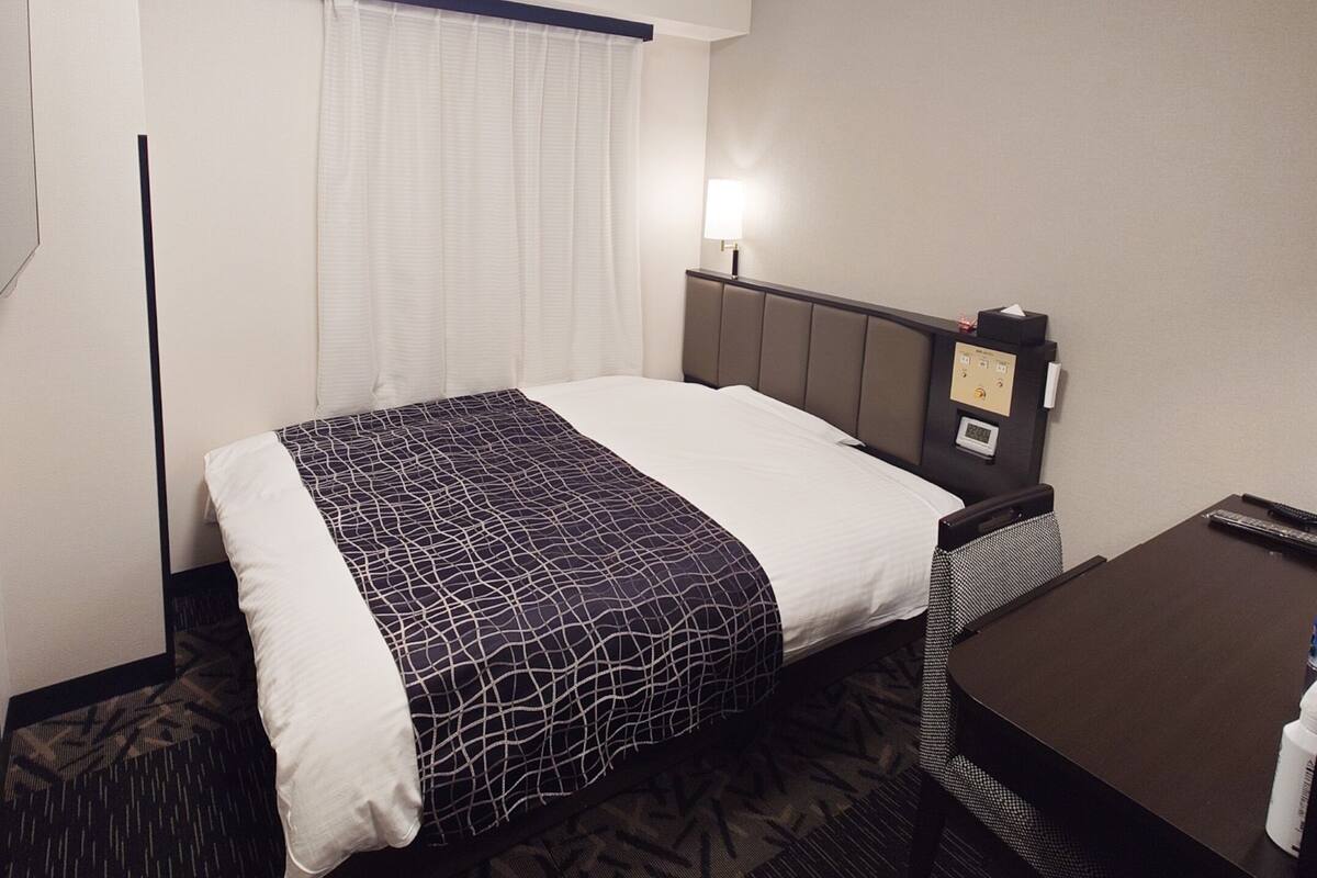 Une chambre d’hôtel équipée d’un lit, d’une table de chevet, d’une lampe et d’un panneau de commande.
