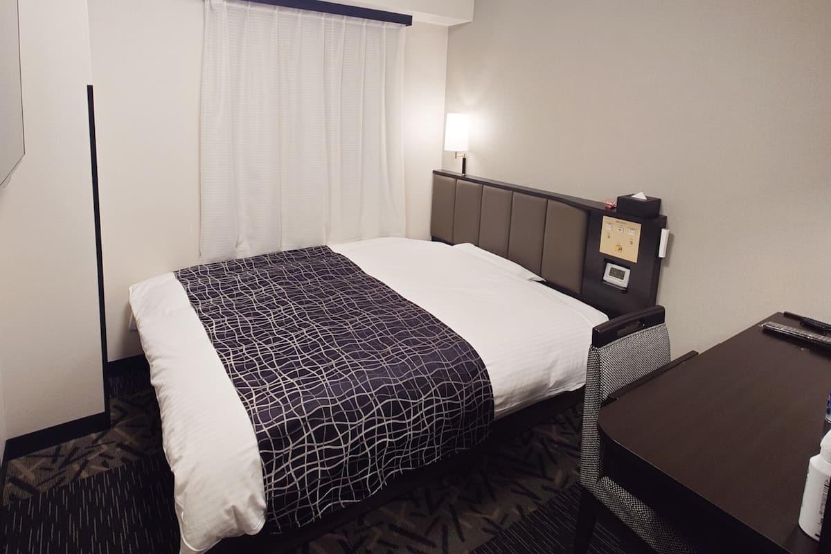 Une chambre d’hôtel équipée d’un lit, d’une table de chevet, d’une lampe et d’un panneau de commande.