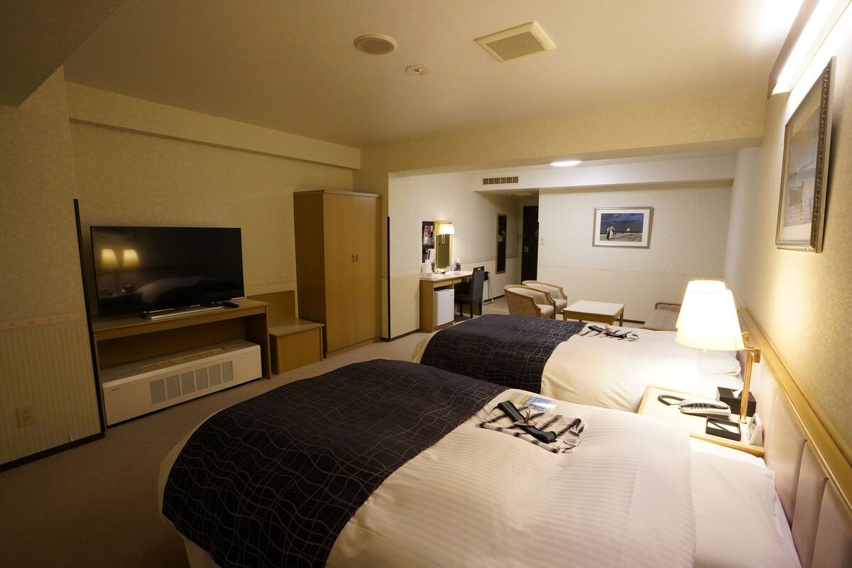 Une chambre d’hôtel avec deux lits, une télévision, un bureau, une chaise et une lampe.