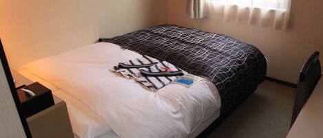 A neatly made bed with a patterned bedspread, a white pillow, and a striped item on the bed. There is a small bedside table with a tissue box on it.