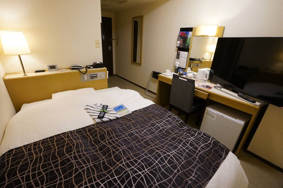 Une chambre d’hôtel équipée d’un lit, d’un bureau, d’une télévision et d’un réfrigérateur.
