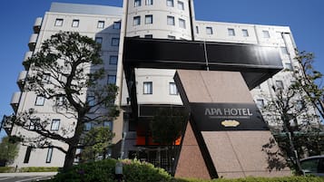 APA Hotel features a modern design with a prominent sign and lush green surroundings.