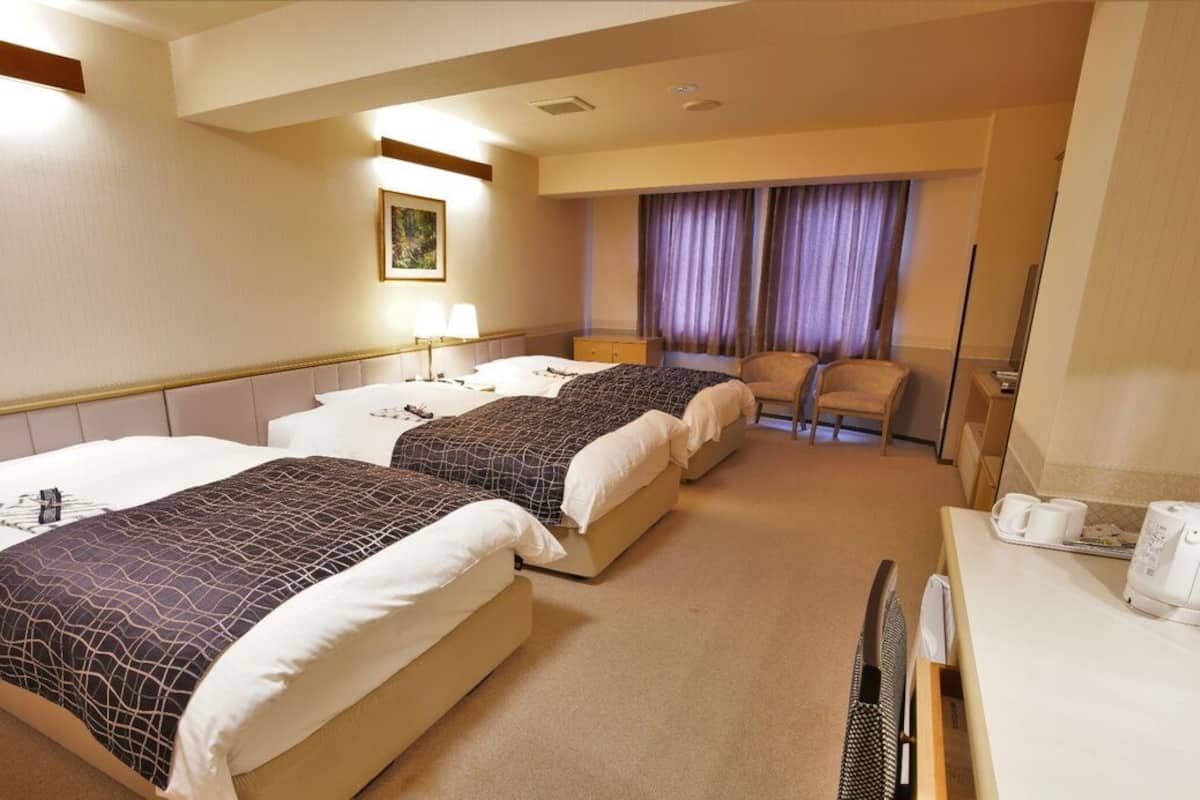 Une chambre d’hôtel avec deux lits, un bureau avec une machine à café, une chaise, une fenêtre avec des rideaux et un tableau au mur.