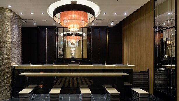 Een moderne hotel lobby met een centraal gelegen receptiebalie, een grote kroonluchter en een decoratieve kolom.