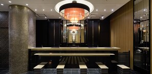 A modern hotel lobby with a central reception desk, a large chandelier, and a decorative column. - APA Hotel Sagamihara Kobuchi Station Mae (Sagamihara)