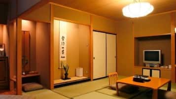 A traditional Japanese-style room with tatami flooring, a low table with cushions, a television, and sliding doors.