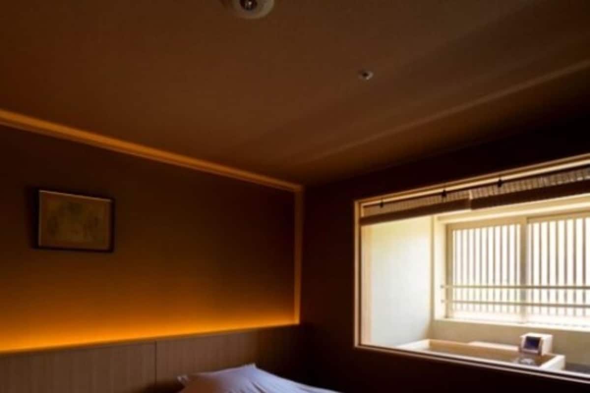 A hotel room with a bed, bedside table, and a window with blinds.