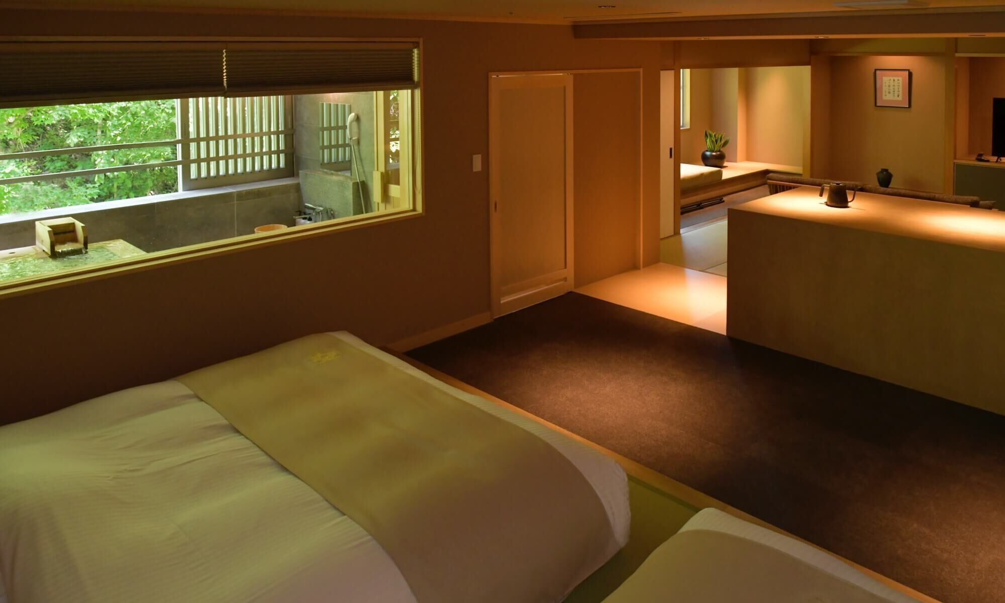 Une chambre d’hôtel avec un lit, une petite table, une fenêtre donnant sur un espace verdoyant et une salle de bain avec douche.