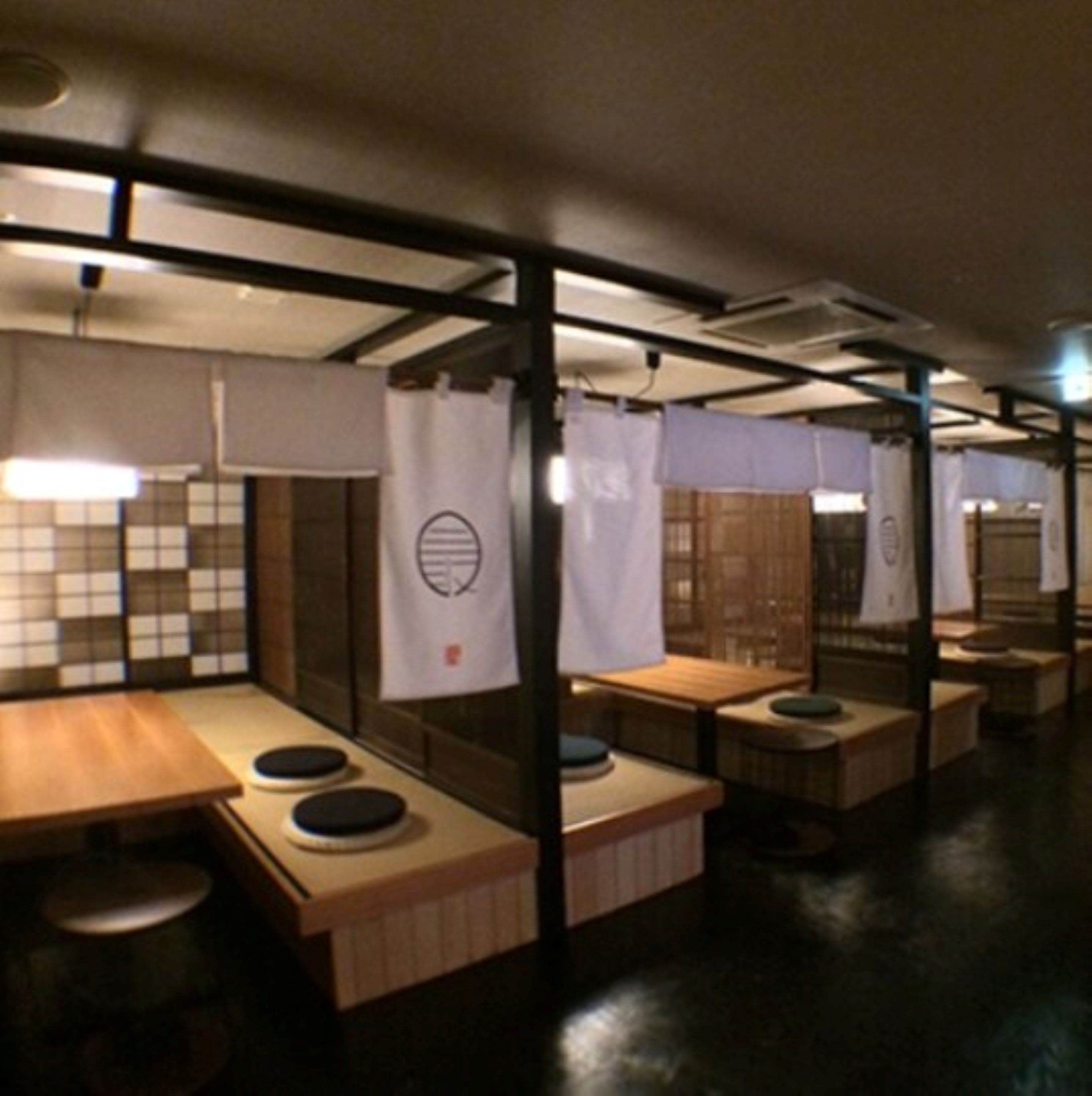 A row of wooden tables with stools, each separated by a curtain with a logo.