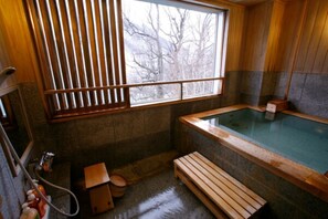 Un bain traditionnel de style japonais, avec un banc en bois, une fenêtre avec des stores et un mur en pierre.