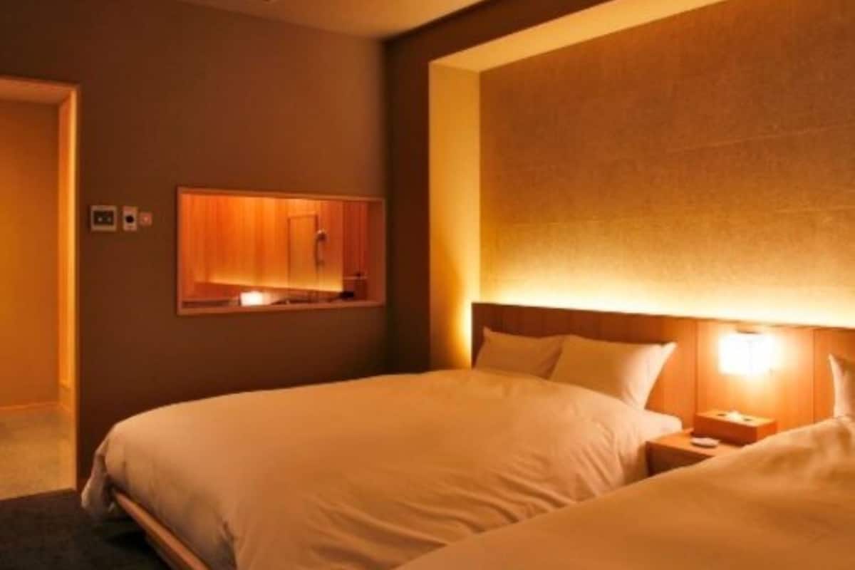 A hotel room with two beds, a wooden headboard, a nightstand, and a wall-mounted cabinet.