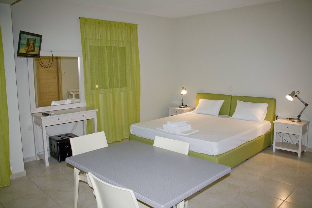 A hotel room with a bed, a desk, a chair, a nightstand, and a lamp.