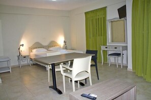 A hotel room with a bed, a desk, a chair, a small table, and a TV. - Fournia Village (Andravida-Kyllini)