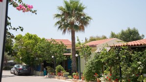 A residential street with a parked car, a palm tree, and houses with red-tiled roofs and potted plants. - Fournia Village (Andravida-Kyllini)