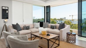 A modern living room with a beige sectional sofa, two armchairs, a wooden coffee table, and a small side table. Large windows offer a view of the cityscape. - Warwick 504 (Cape Town)