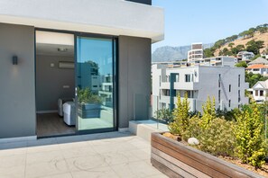 A modern apartment with a glass door leading to a balcony, a wooden planter, and a view of surrounding buildings and hills. - Warwick 504 (Cape Town)