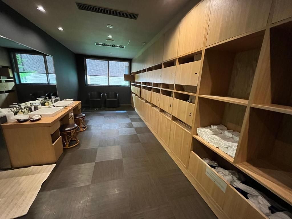A hotel room with a checkered floor, a wooden vanity with a mirror, and a large wooden wardrobe with multiple shelves.
