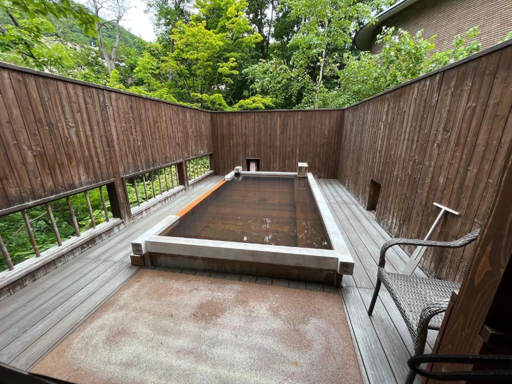 Eine Holzterrasse mit einem Whirlpool, umgeben von einem Holzzaun und Bäumen.
