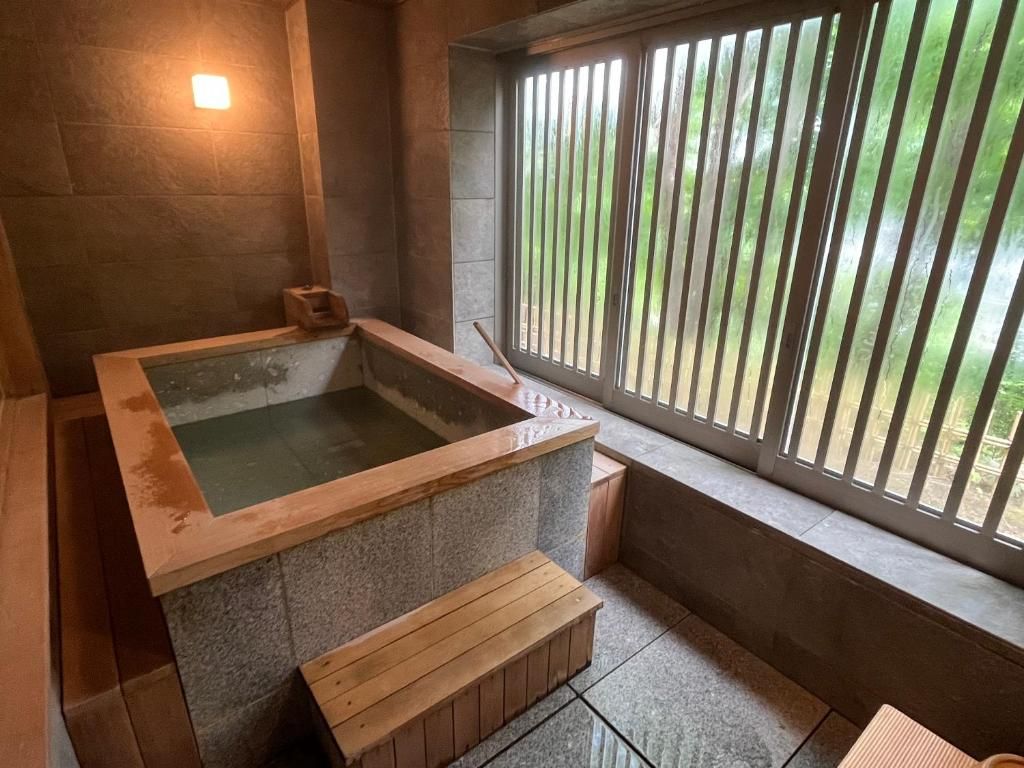 Un jacuzzi con revestimiento de piedra, bancos de madera y una ventana con persianas verticales.