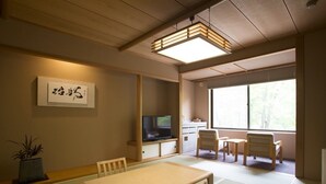 A traditional Japanese room with tatami flooring, a low table, chairs, a television, and a window with a view of trees. - Kuriyasuizan (Sapporo)