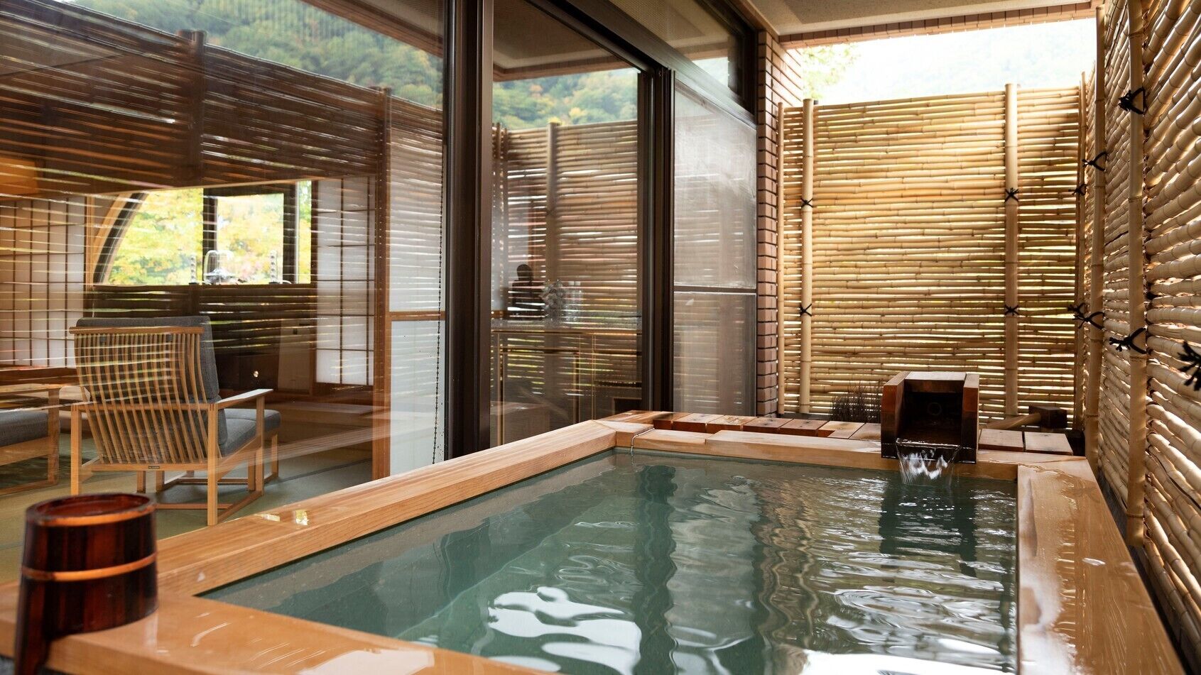A hot tub with a wooden deck, a chair, and a bamboo wall.