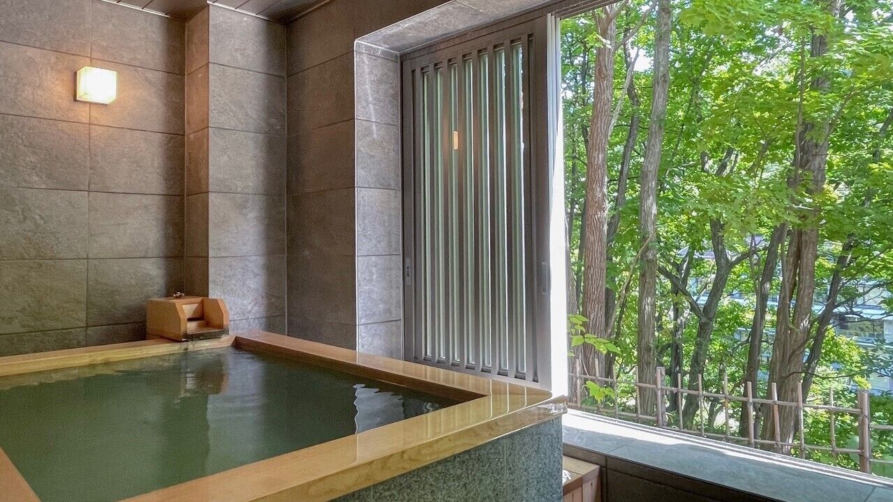 A spa area with a hot tub, stone walls, and a view of trees through a window.