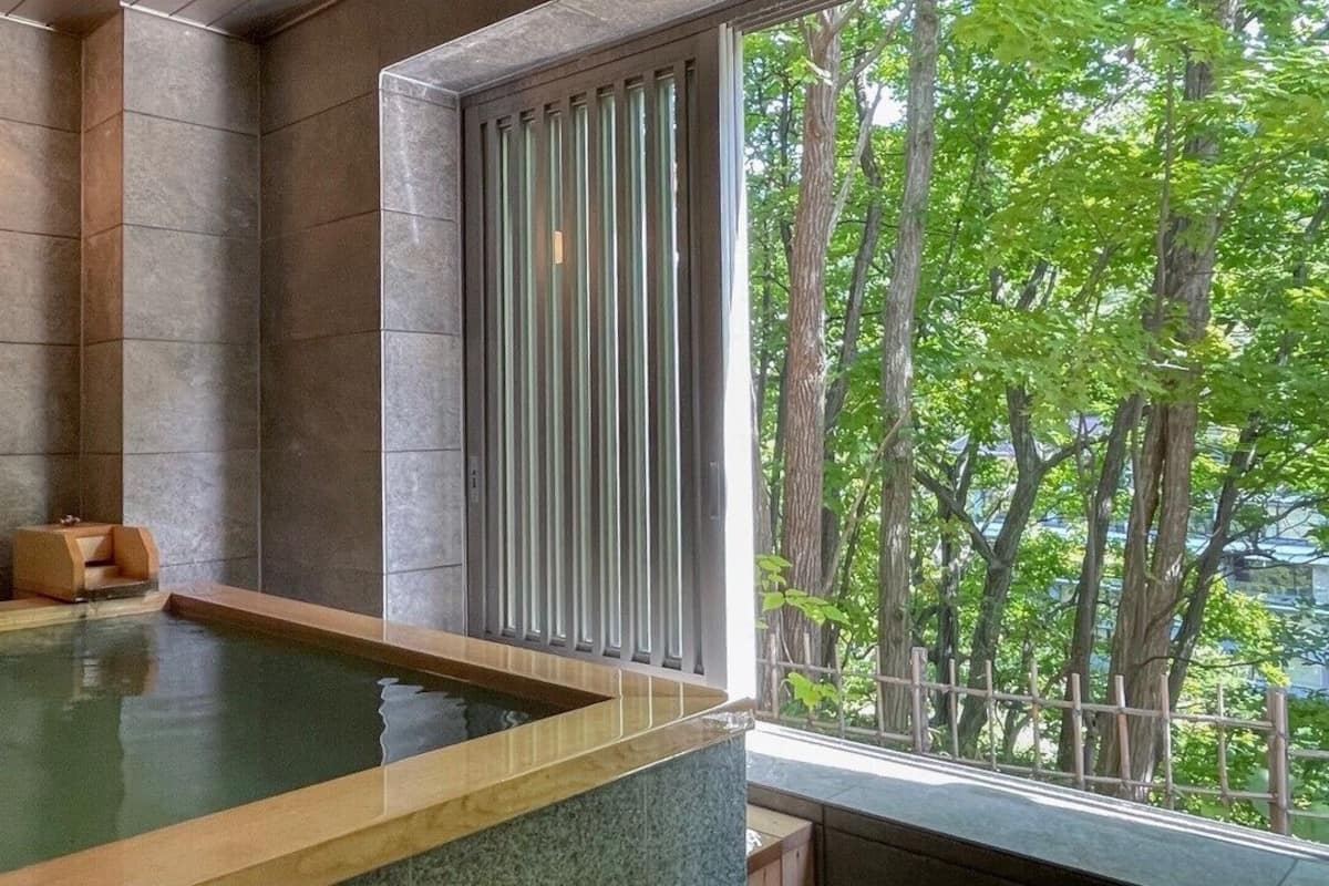 Uma área de spa com hidromassagem, paredes de pedra e vista para árvores através de uma janela.