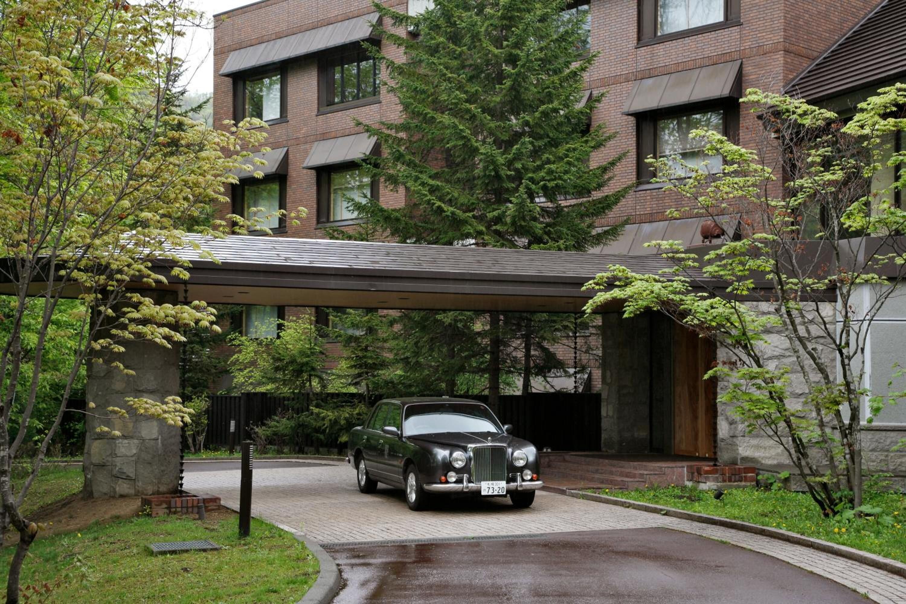 A black convertible car parked in front of a modern brick building with a covered driveway.