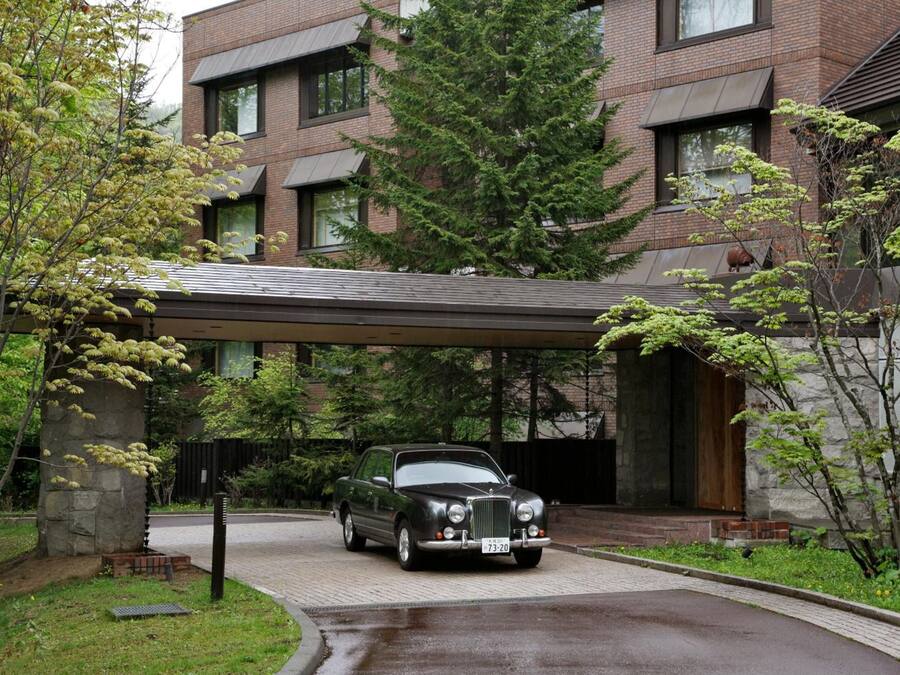 A black convertible car parked in front of a modern brick building with a covered driveway.