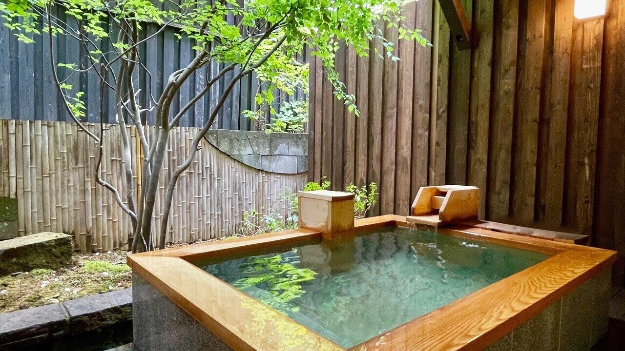 A hot spring bath area with wooden benches, a bamboo fence, and a wooden wall.