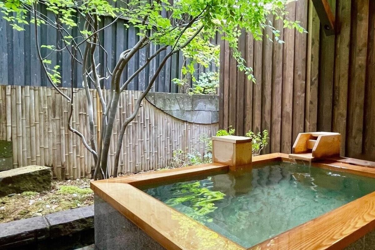 Un espace de baignade dans une source thermale, avec des bancs en bois, une clôture en bambou et un mur en bois.