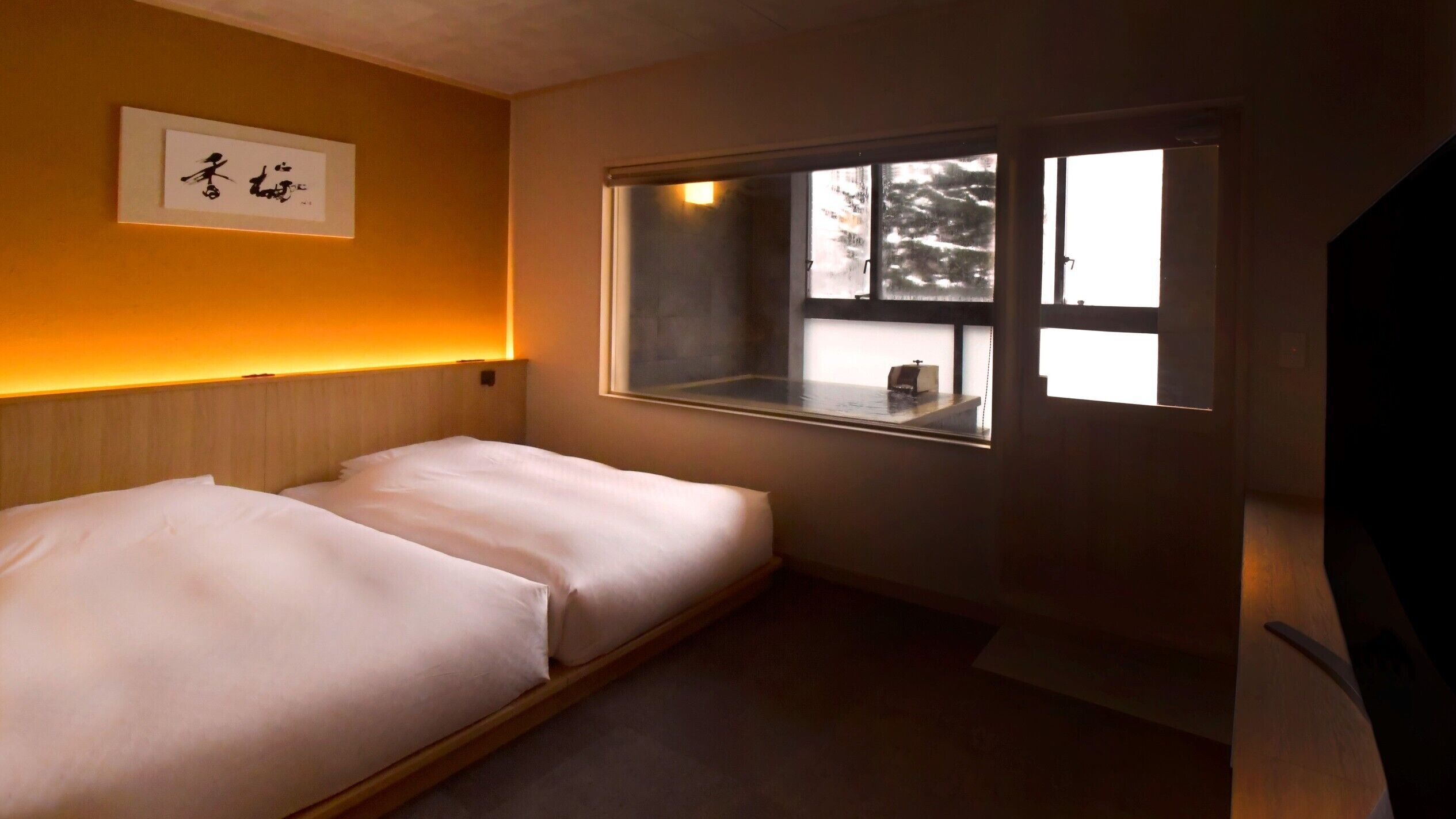 A hotel room with a bed, a window, and a framed artwork on the wall.