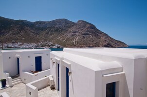 Un edificio blanco con puertas y ventanas azules, con montañas y el mar de fondo.
