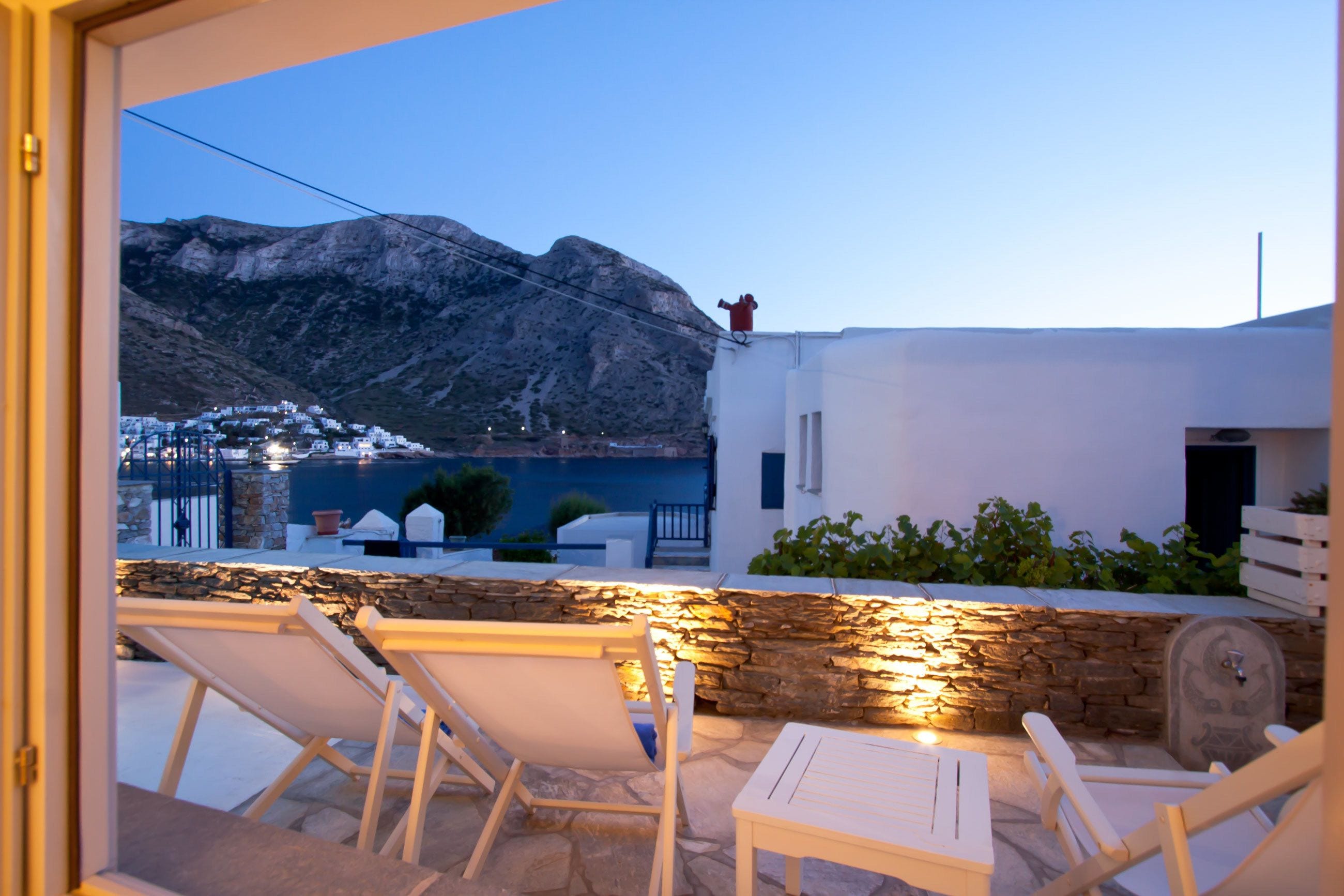 A terrace with stone walls, white furniture, and a view of a mountainous landscape.