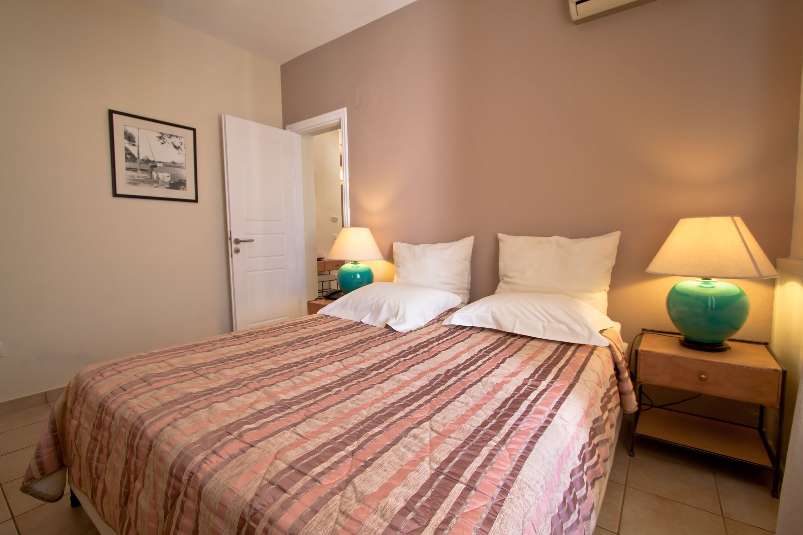 Een slaapkamer met een bed, twee bedlampen, een nachtkastje en een ingelijst schilderij aan de muur.