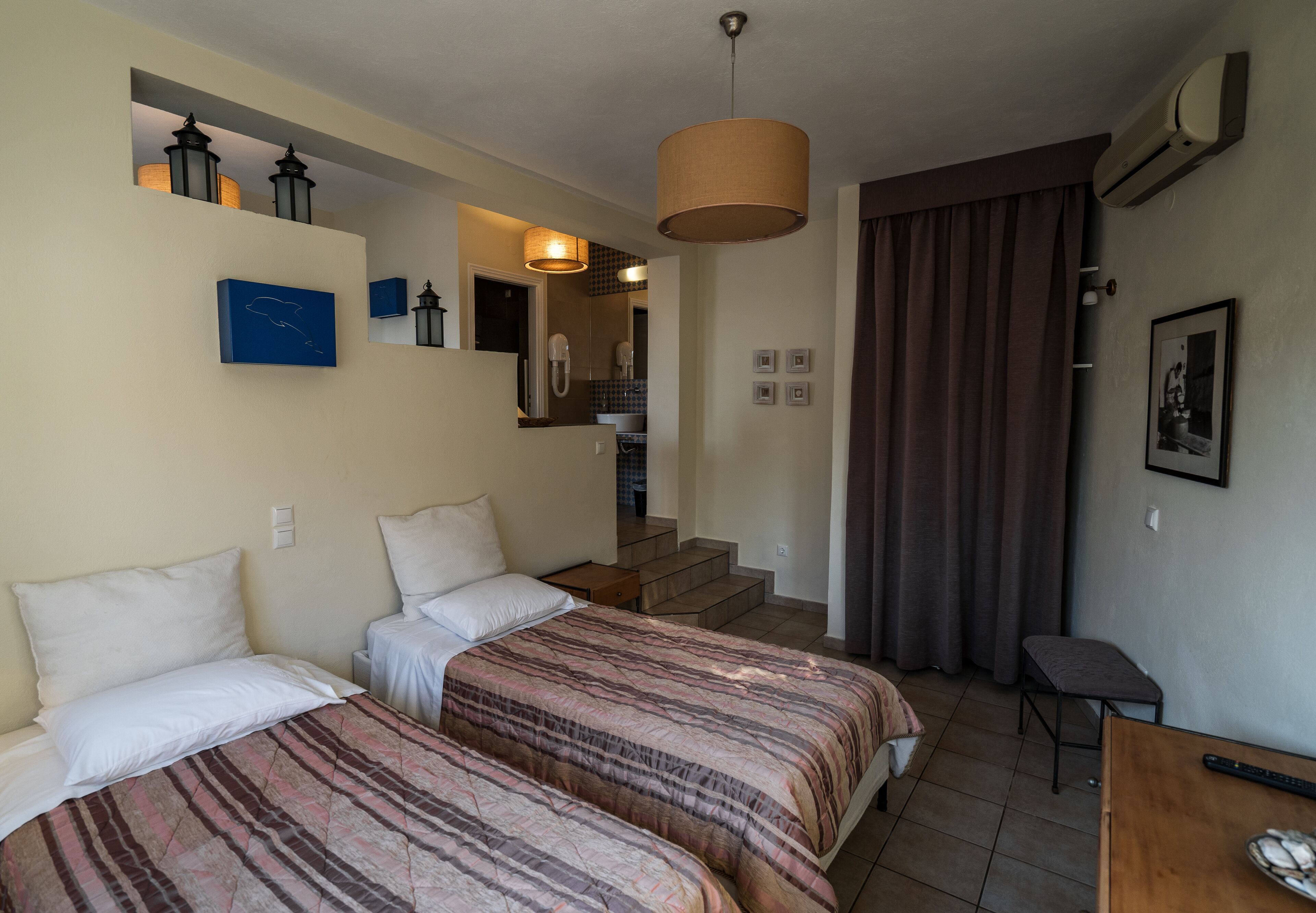A hotel room with two beds, a desk, a chair, a staircase, and a bathroom visible in the background.