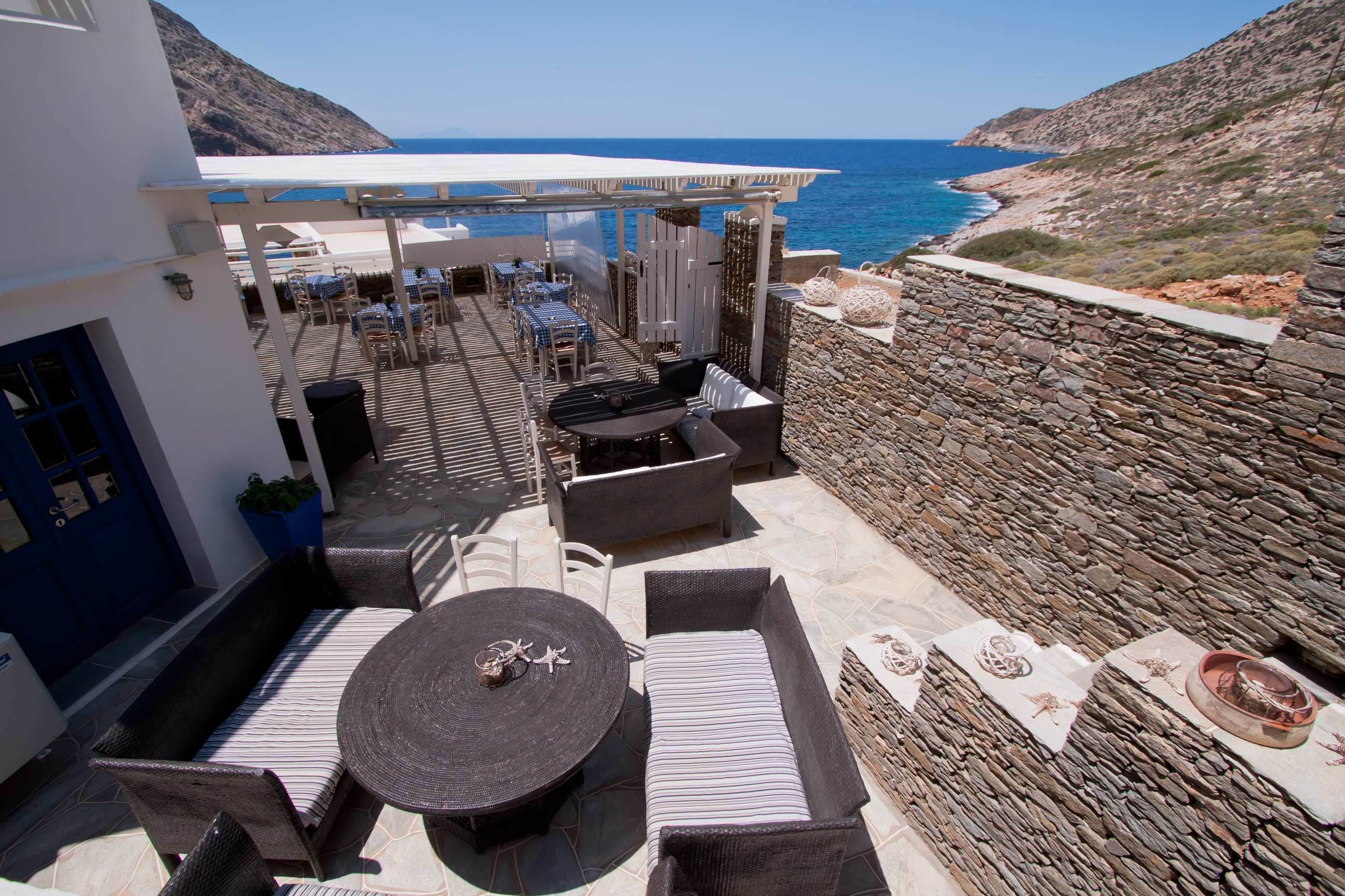 A terrace with outdoor seating, a stone wall, and a view of the sea.