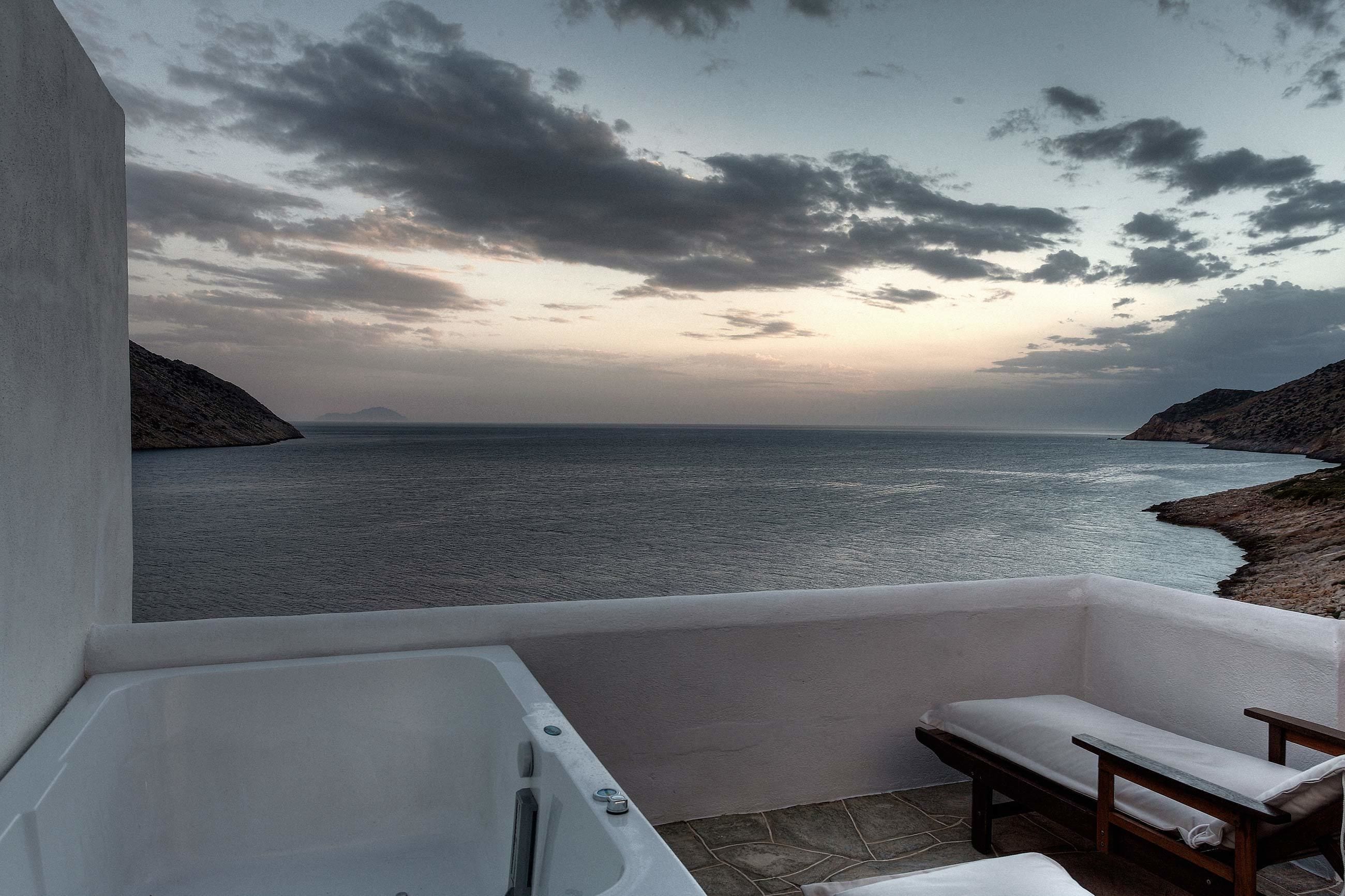 Un balcón con vista al mar, una bañera y un banco de madera.