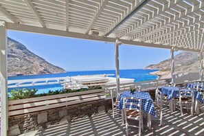 An outdoor seating area with tables and chairs, overlooking a coastal landscape with a clear blue sea and a mountainous backdrop. - Delfini Hotel (Sifnos)
