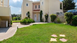 A modern two-story building with a flat roof, a central entrance, and a small garden area with stepping stones. - Hidden garden Rhodes Apartments (Rhodes)