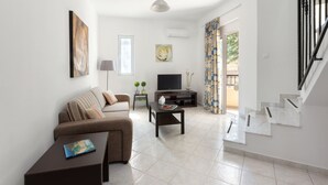 A modern living room with a sofa, coffee table, TV, and staircase. - Hidden garden Rhodes Apartments (Rhodes)