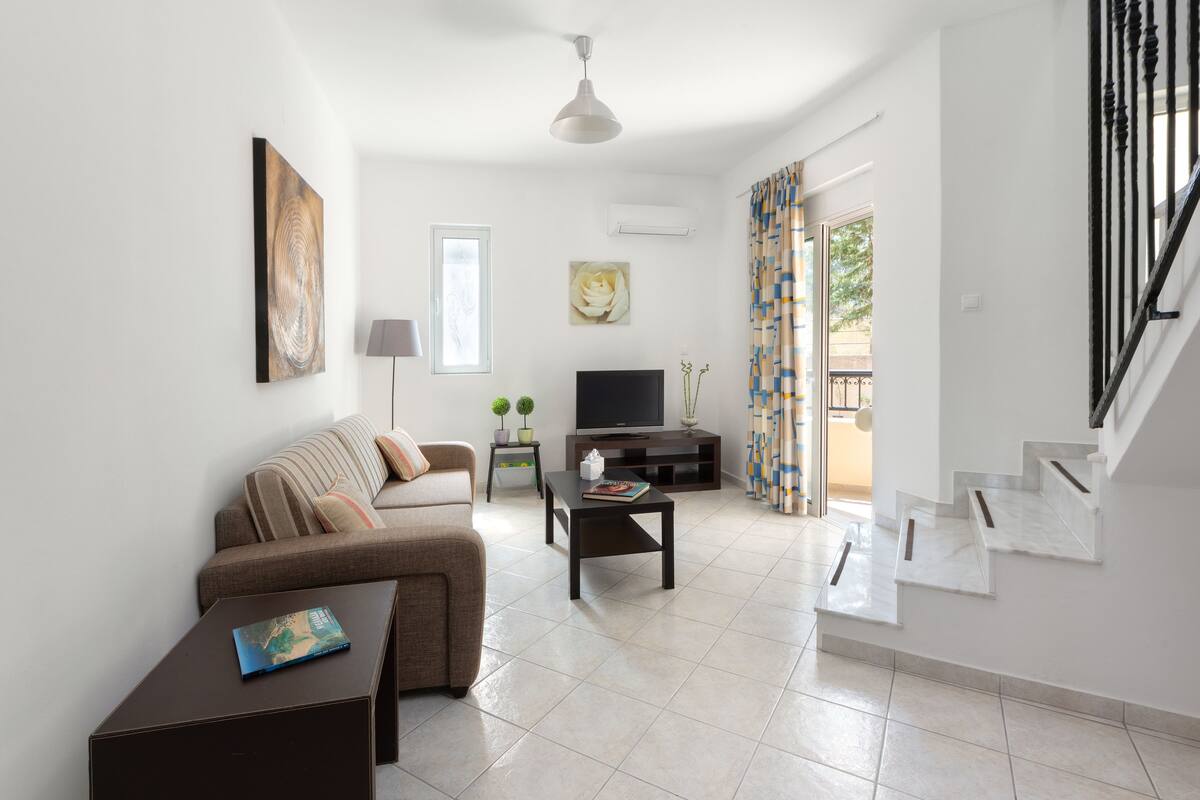 Ein modernes Wohnzimmer mit Sofa, Couchtisch, Fernseher und Treppe.