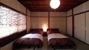 A traditional Japanese-style room with tatami flooring, two beds with brown bedding, a hanging light fixture, and sliding doors. - Yanaka No Taisuke (Gujo)